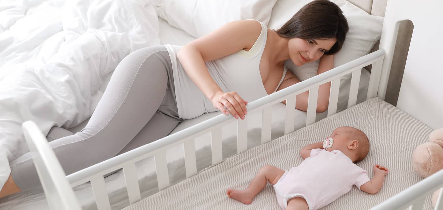 Maman allougé sur son lit avec bébé endormi dans son cododo