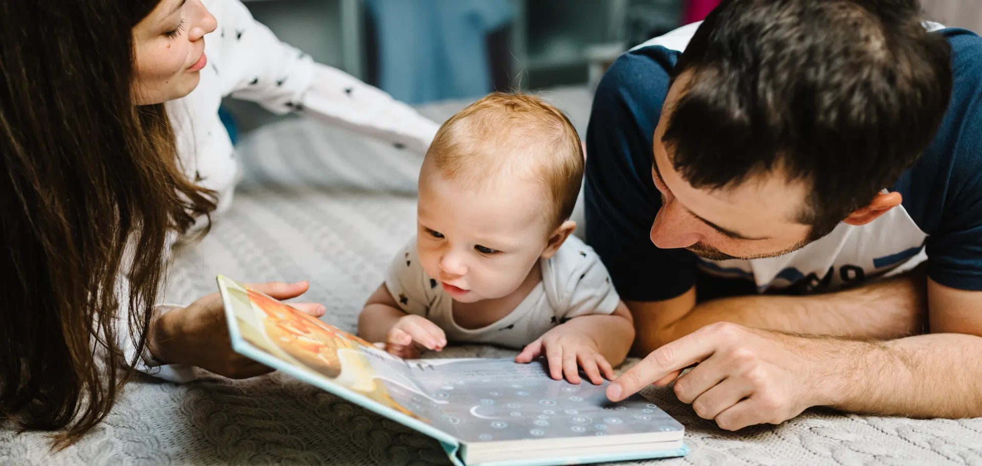 Bébé avec ses parents allongés devant un livre