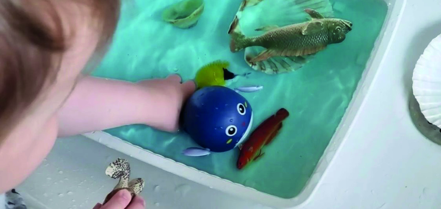 enfant avec jouets et main dans un bac d'eau 