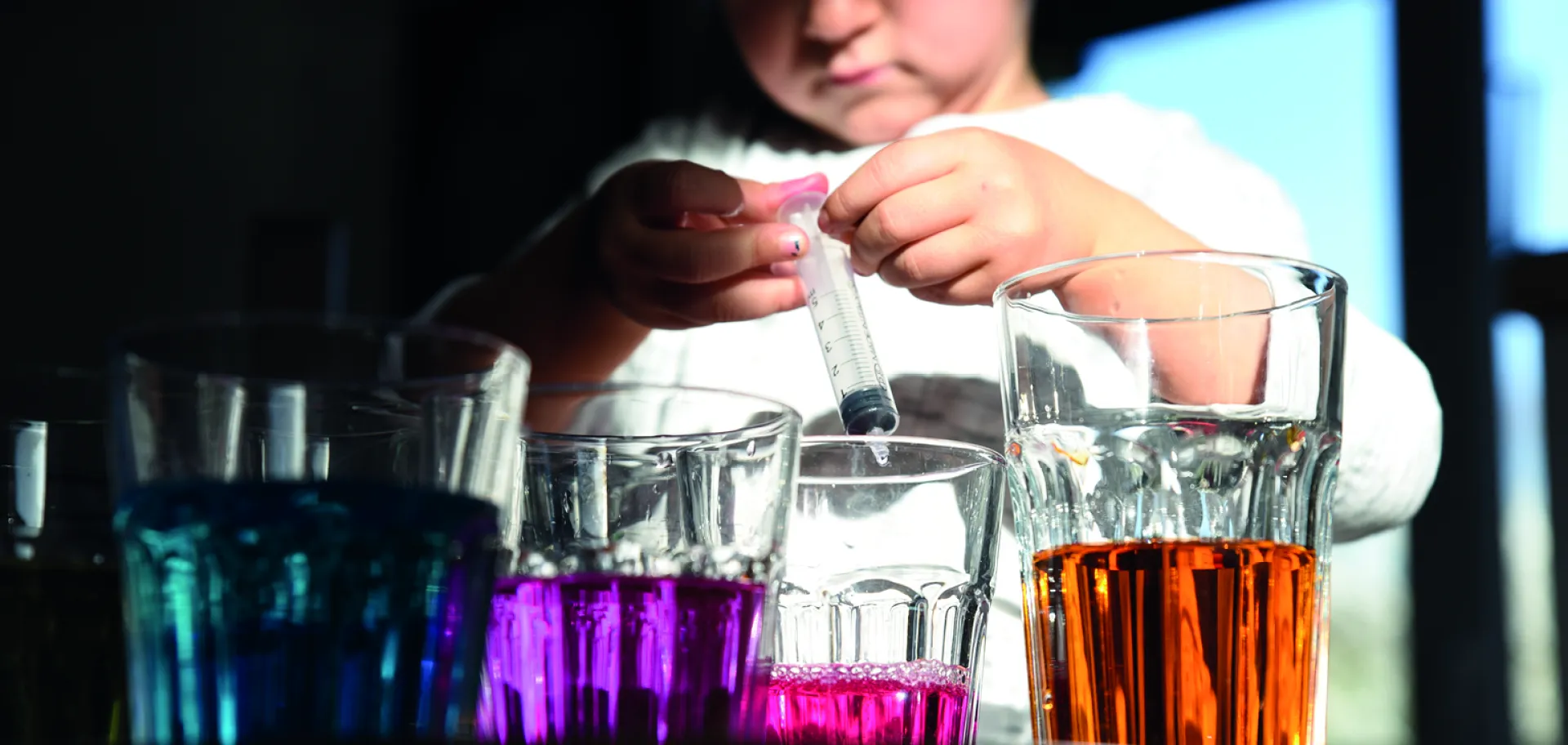 enfant utilisant une pipette et  verres de liquides de différentes couleurs